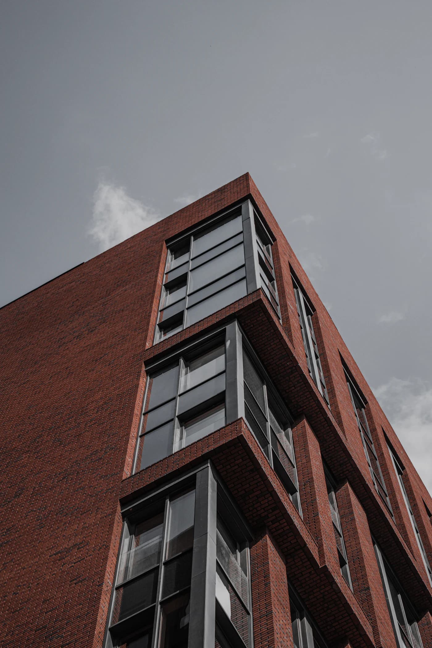 Moderne Wohnfassade aus rotem Backstein vor grauem Himmel, von unten gesehen